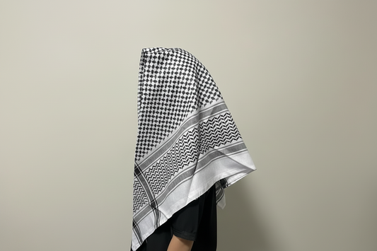 Person wearing a black and white checkered headscarf against a plain wall.